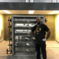 A Kelair shop worker smiles while standing next to a large louver damper.