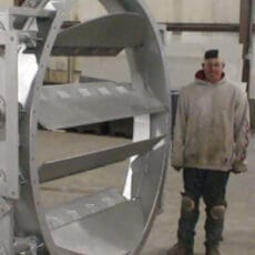 A Kelair shop worker smiles while standing next to a massive industrial damper.
